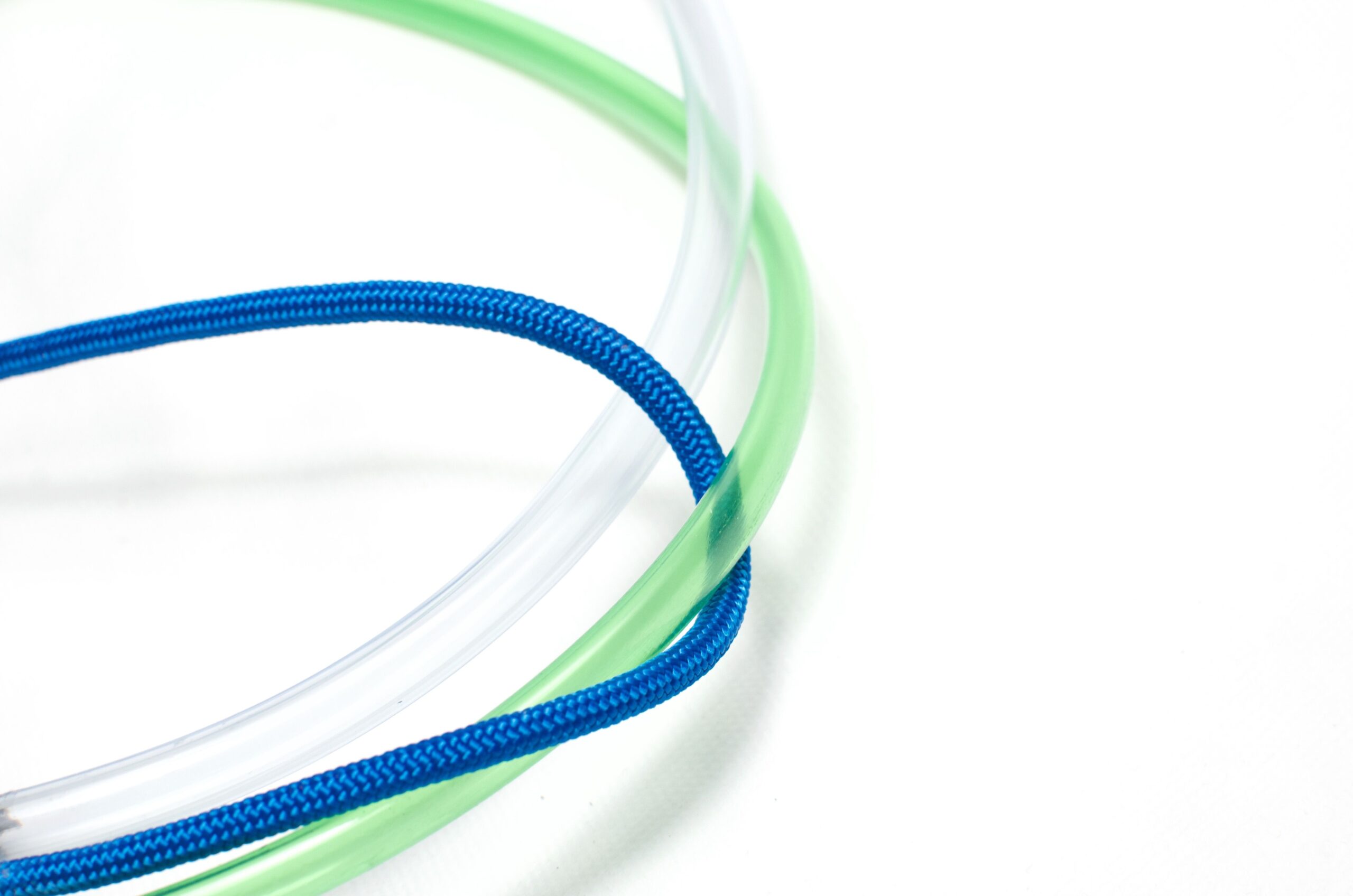 High angle of blue cable rope intertwined with transparent white and green plastic tubes placed on white surface in daylight