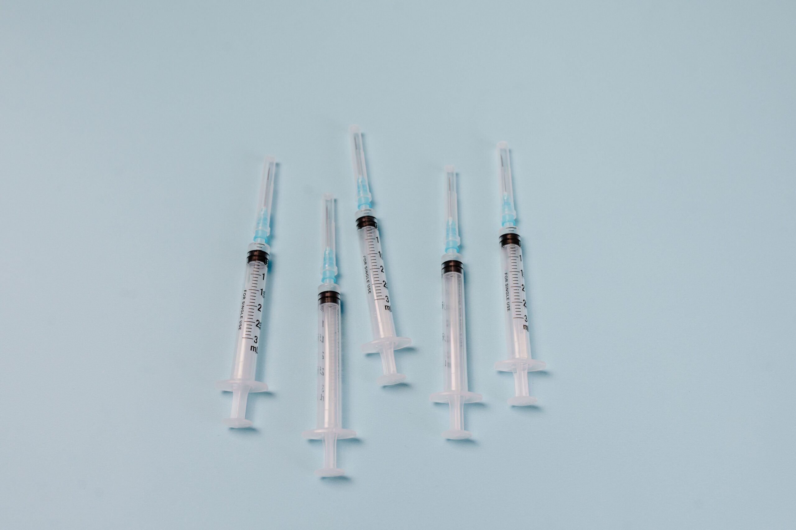 Close-up of sterile syringes arranged on a light blue surface, ideal for medical themes.